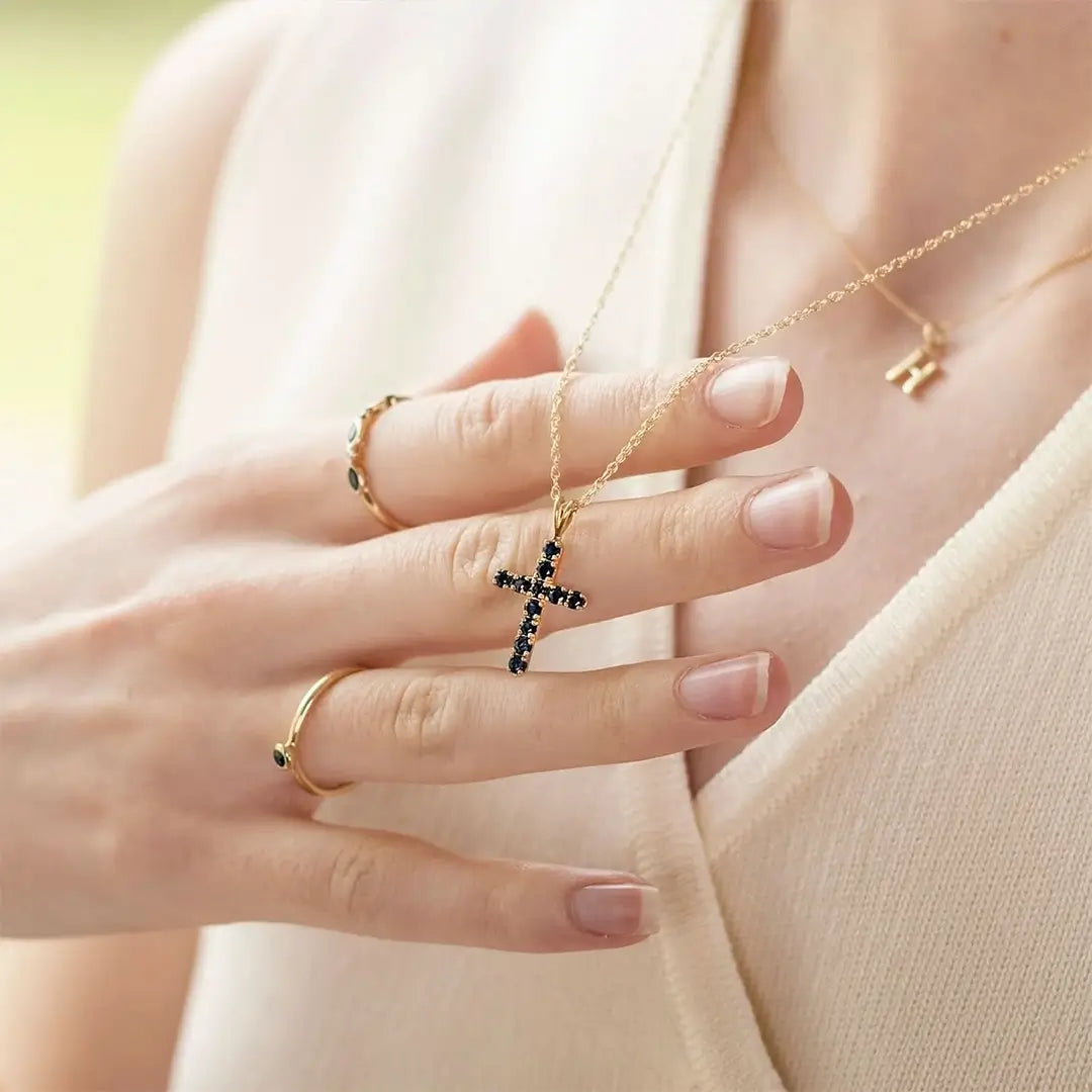 Gold sapphire cross necklace held against neutral knit, gemstone cross pendant styling