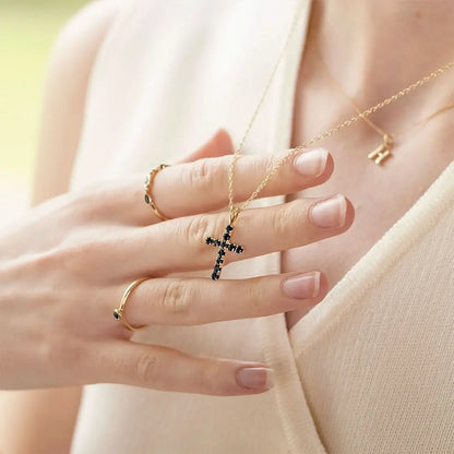 Gold sapphire cross necklace held against neutral knit, gemstone cross pendant styling