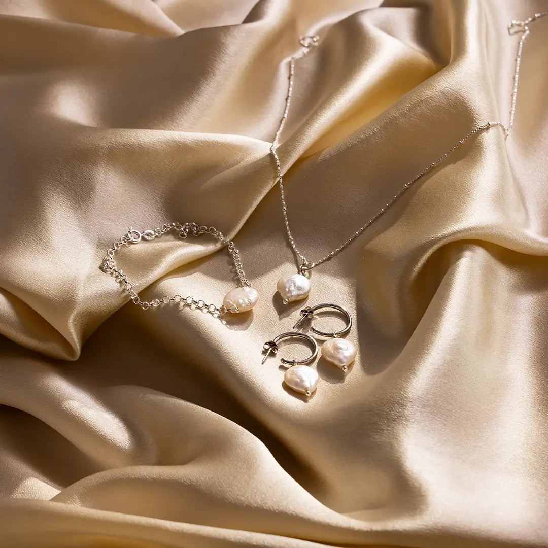 Jewelry set of ivory coin pearls in including a necklace, bracelet, and earrings on beige satin  fabric