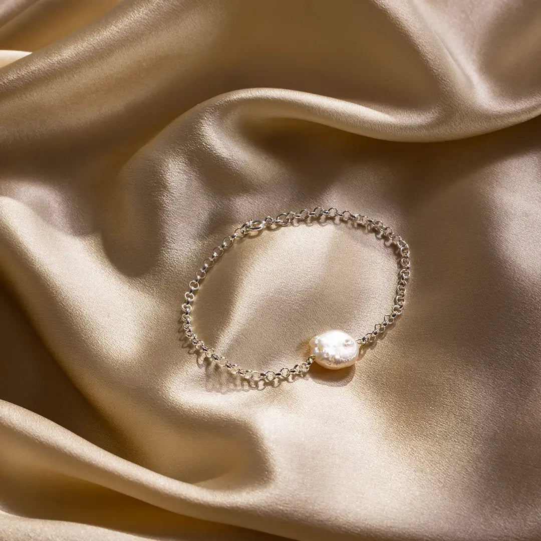 Sterling silver coin pearl bracelet displayed on gold satin fabric, highlighting natural freshwater pearl detail