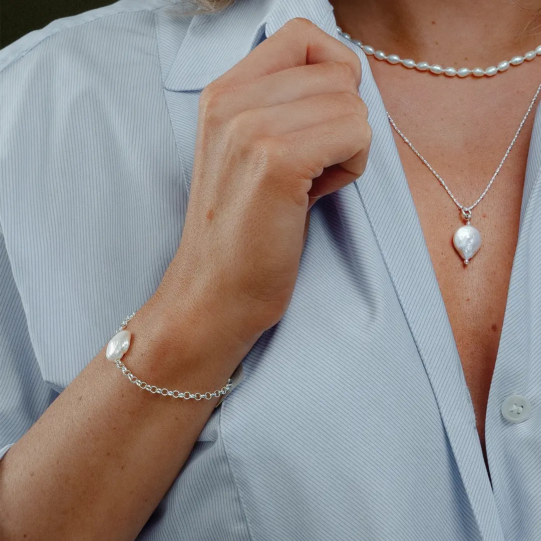 Close-up of silver coin pearl bracelet worn with matching pearl necklace and pendant, layered jewellery styling