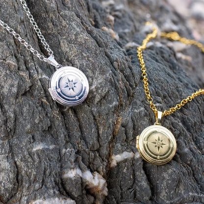 Silver and gold compass locket necklaces displayed on textured rock, highlighting contrast between metal finishes