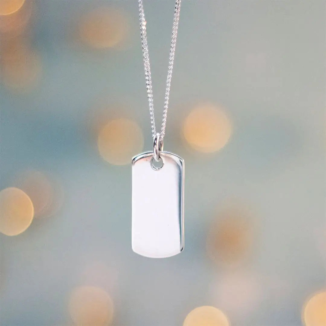 Sterling silver dog tag necklace suspended against soft bokeh background, polished pendant highlighting engraving surface.