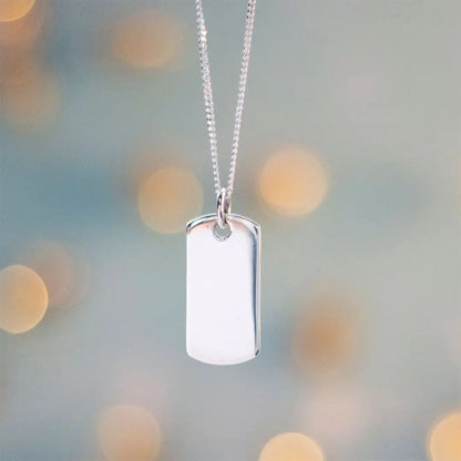 Sterling silver dog tag necklace suspended against soft bokeh background, polished pendant highlighting engraving surface.