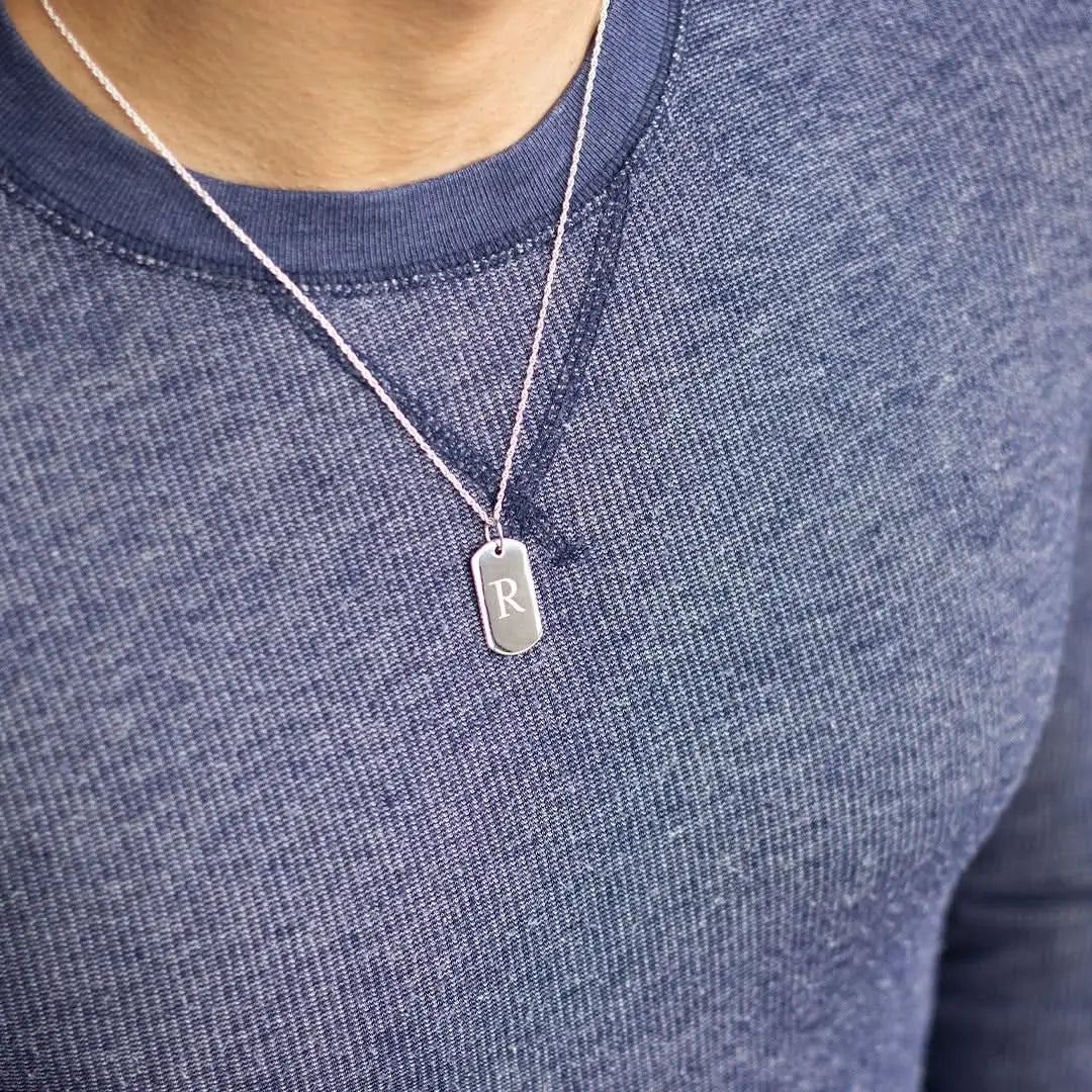 Close-up of engraved sterling silver dog tag necklace with initial pendant, worn on belcher chain for personalised styling.