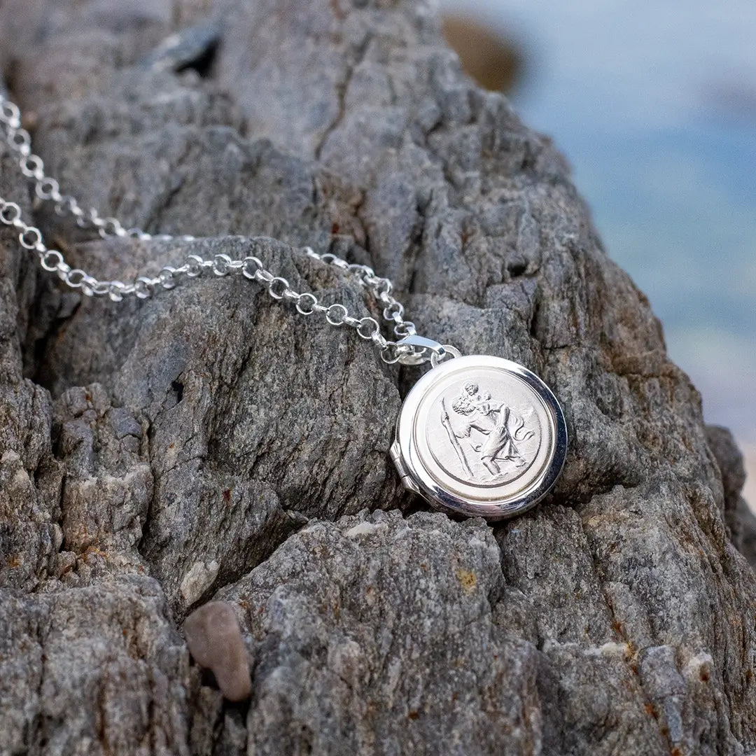 Sterling silver St Christopher locket necklace placed on textured rock in natural outdoor setting