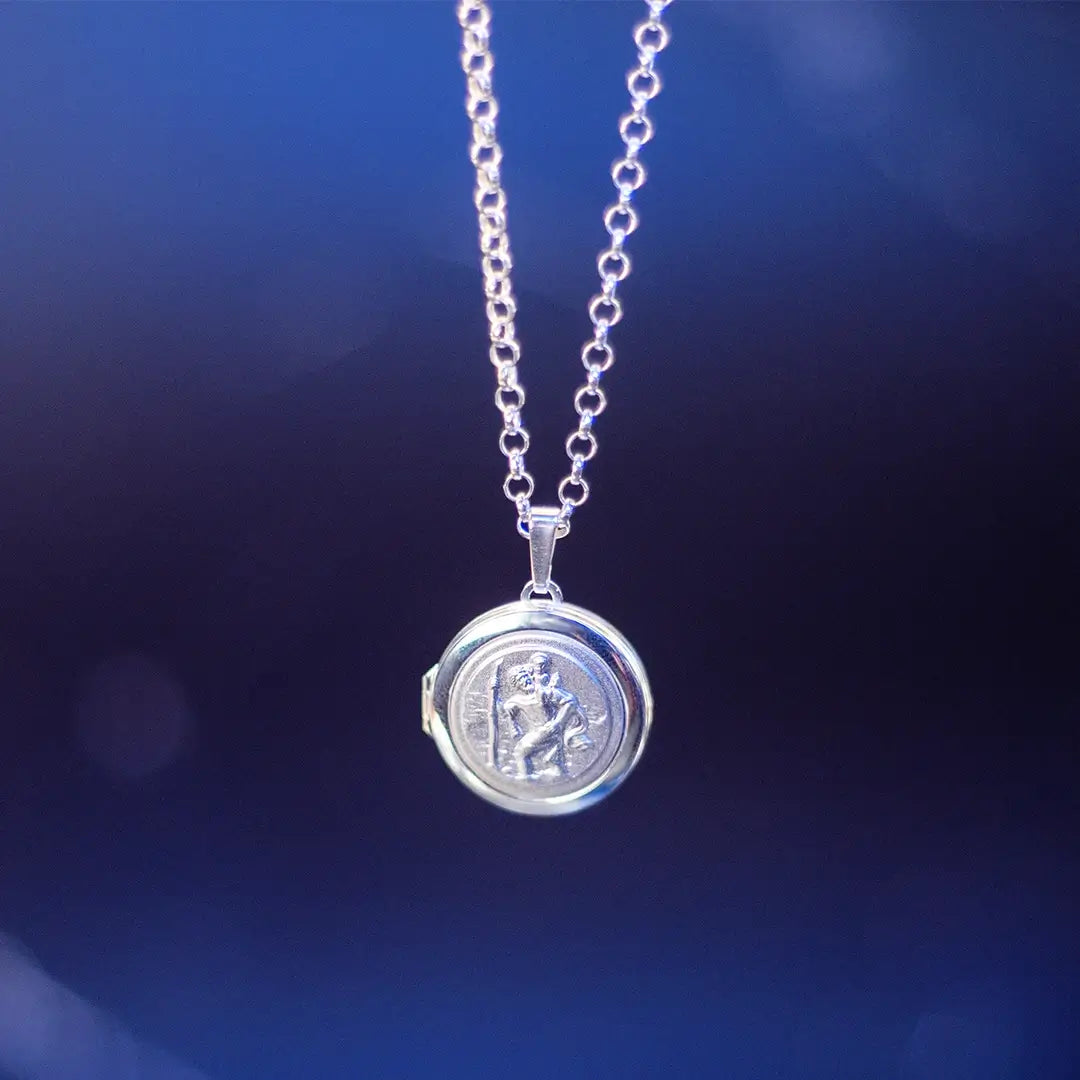 Sterling silver St Christopher locket necklace on a chain against a dark blue softly lit background