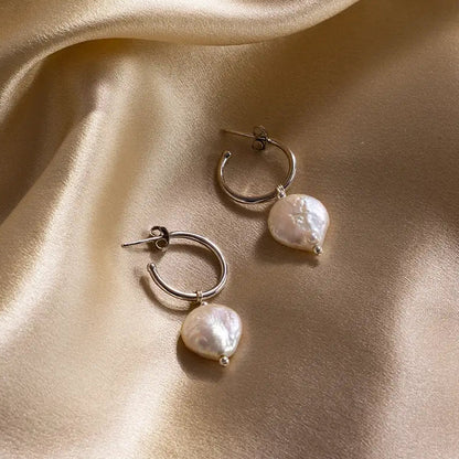 Pair of silver coin pearl hoop earrings displayed on gold satin fabric, highlighting lustre and texture