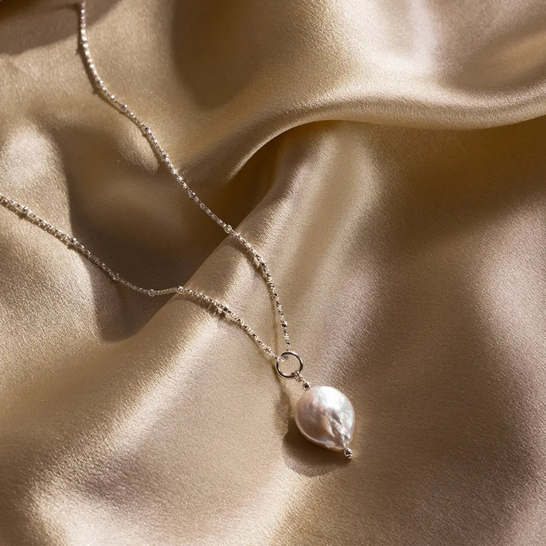 Sterling silver coin pearl pendant necklace on gold satin fabric, highlighting natural freshwater pearl texture