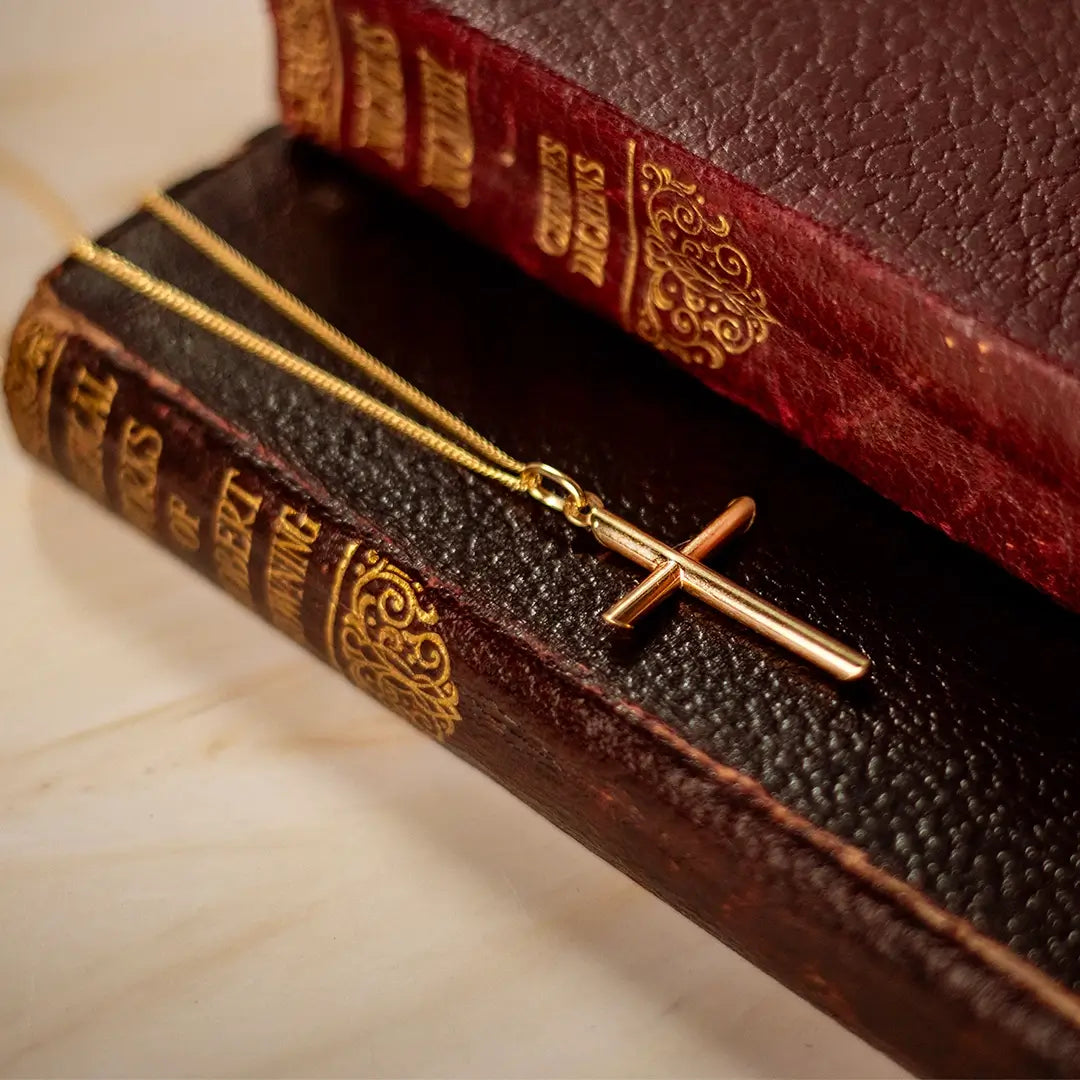 Gold cross pendant necklace styled on stacked vintage books, highlighting warm tones and heritage feel