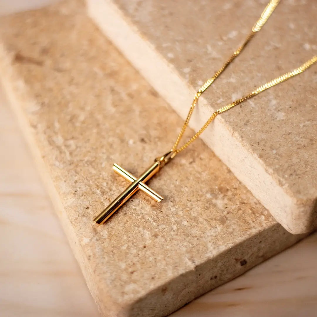 Gold cross pendant necklace resting on a natural stone surface, showcasing the polished finish