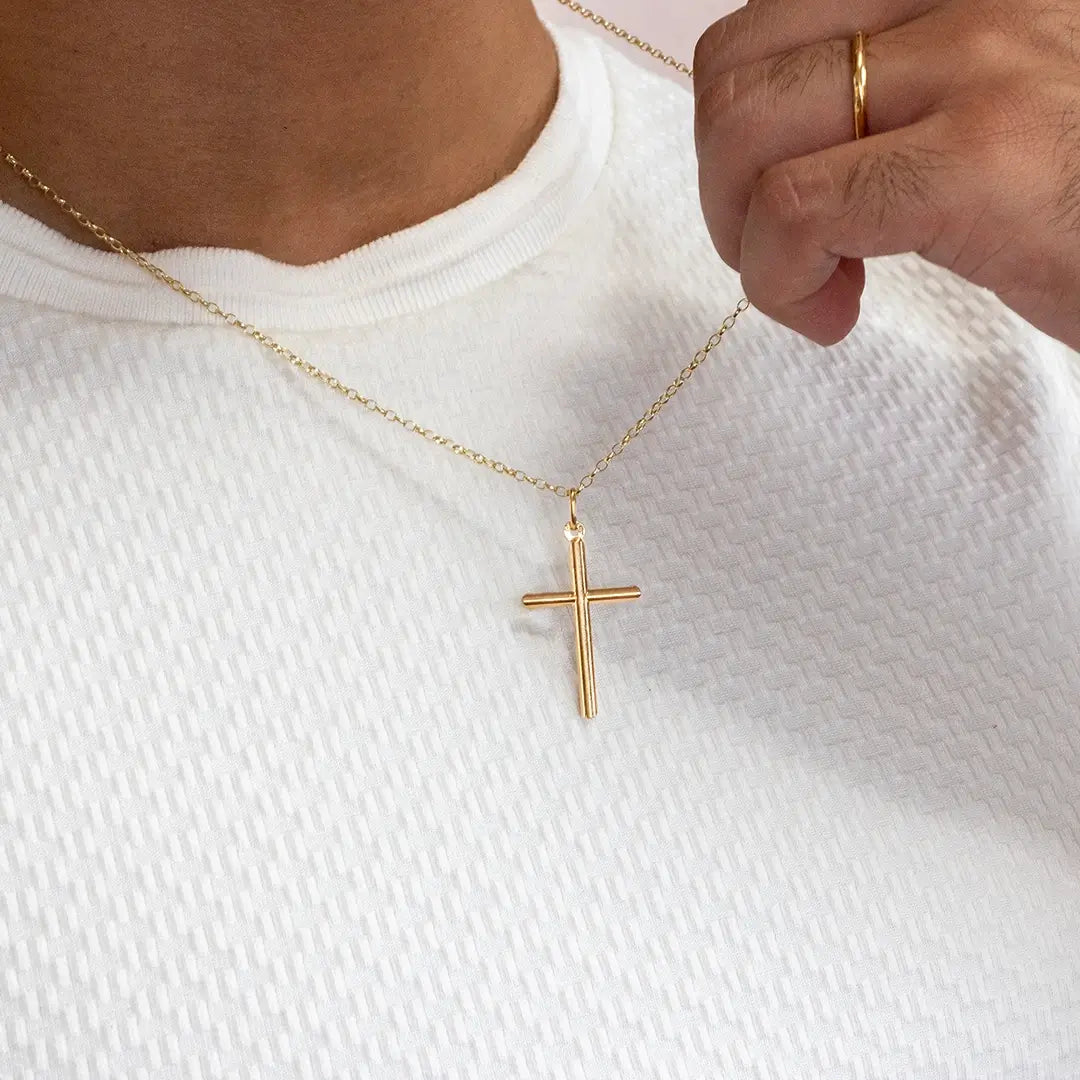 Close-up of a person holding a gold cross pendant necklace while wearing a white textured top