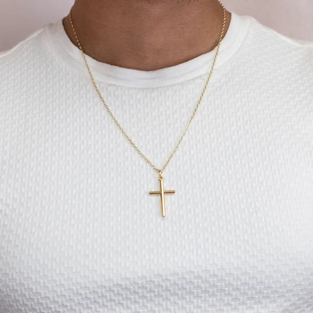 Mid-shot of a person wearing a gold cross necklace on a fine chain styled with a white top
