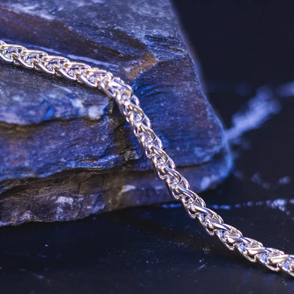 Sterling silver spiga chain necklace draped over textured rock, highlighting strength and woven design