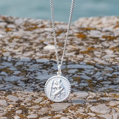 Silver St Christopher necklace laid on textured rock, symbolic protection necklace for travellers