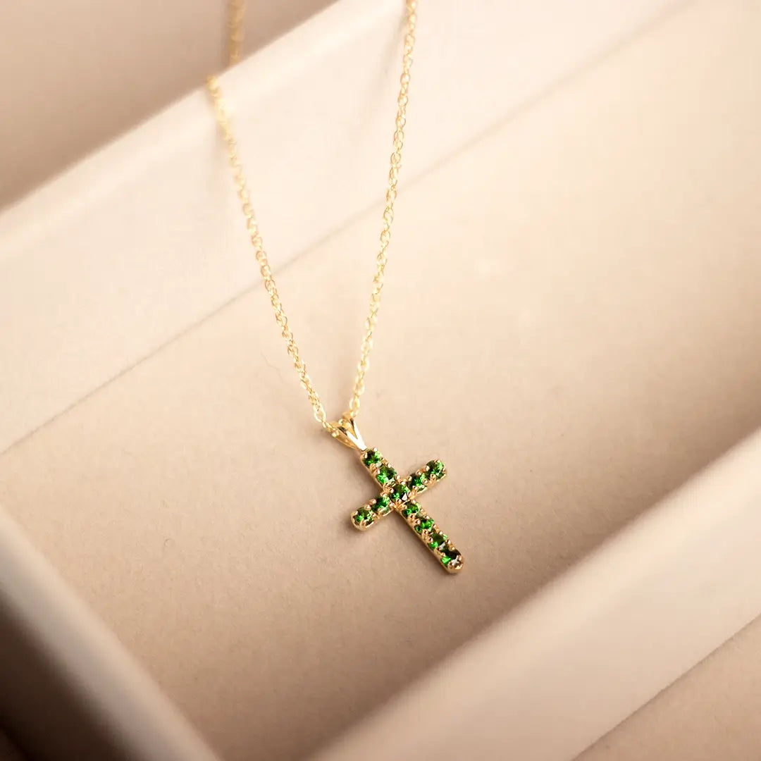 Gold cross necklace set with green tsavorite gemstones displayed in a cream jewellery box