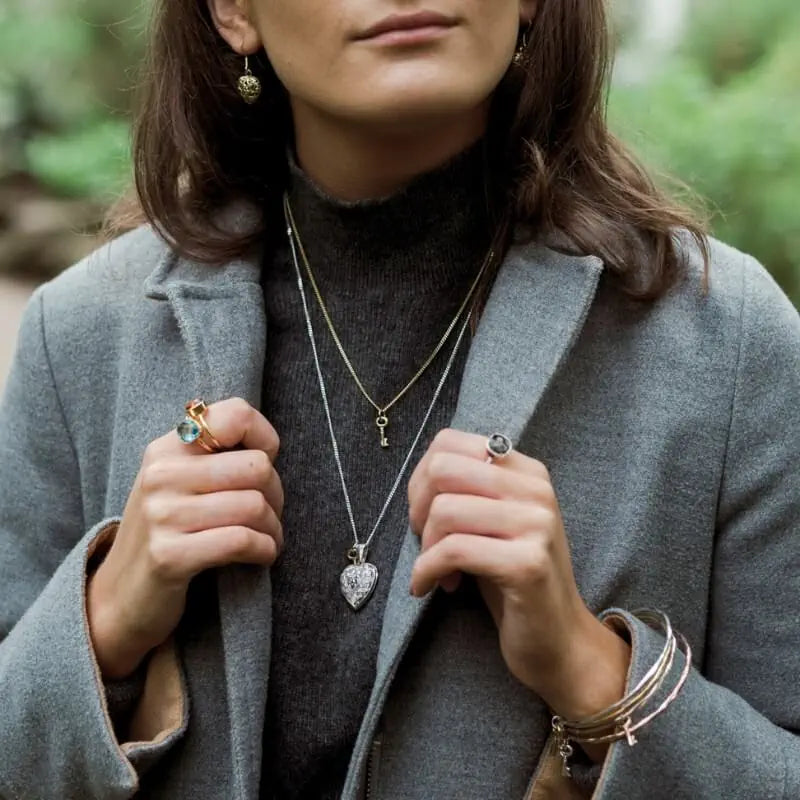 Woman wearing a gray coat with jewellery including a necklace, ring, and earrings.
