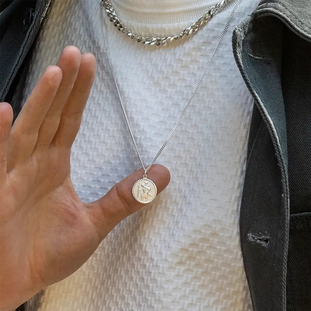 Man holding sterling silver St Christopher necklace, symbolic travel protection pendant close-up
