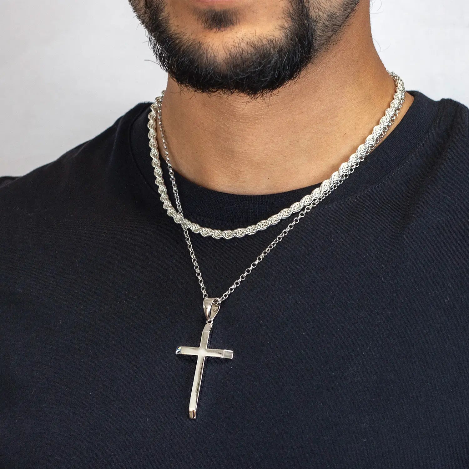 Man wearing a silver cross pendant necklace on a plain background
