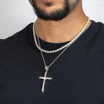Man wearing a silver cross pendant necklace on a plain background