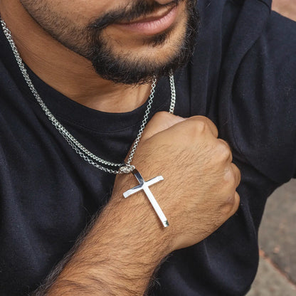 Man wearing a black shirt with a extra large silver cross necklace and chain.