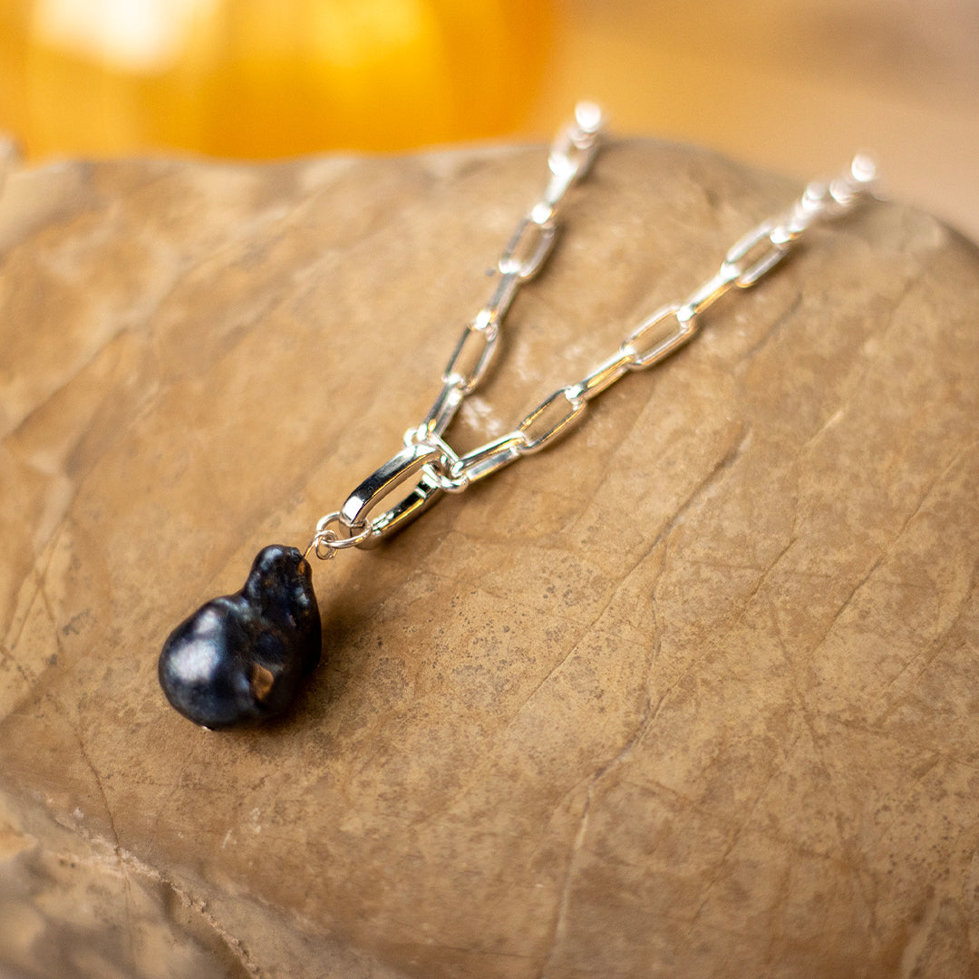 Detachable black pearl photographed on a silver paperclip chain on a rock