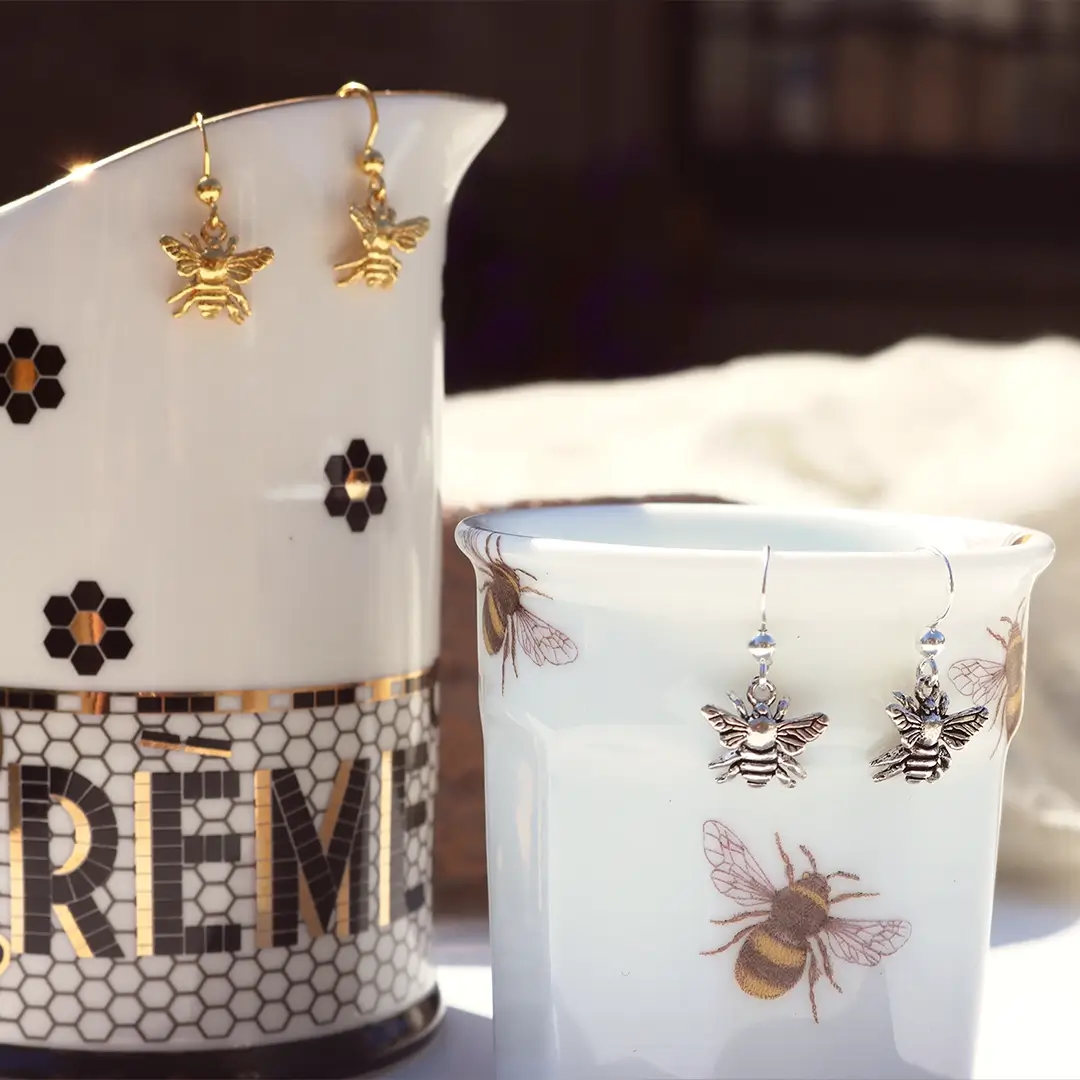 Sterling silver and gold bee drop earrings displayed on honeybee-patterned Emma Bridgewater mugs, highlighting the detailed bee design and nature-inspired styling.