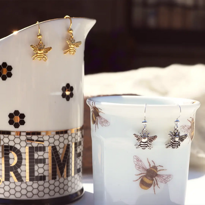Sterling silver and gold bee drop earrings displayed on honeybee-patterned Emma Bridgewater mugs, highlighting the detailed bee design and nature-inspired styling.