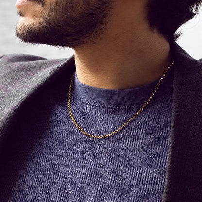 Close-up of a man wearing a gold vermeil belcher chain necklace layered over a navy knit sweater and blazer, showcasing a minimalist men’s jewellery style.