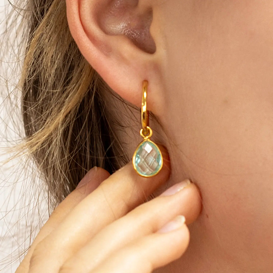 Gold hoop earring with blue topaz drop gemstone, worn on model