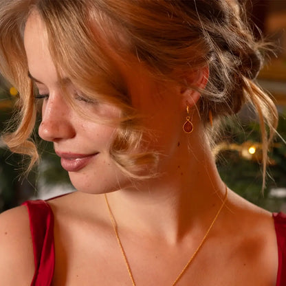Woman in a red dress with curled hair wearing gold hoop earrings with carnelian gemstone drops and a matching gold necklace