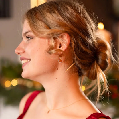 Smiling woman wearing a red dress and gold hoop earrings with carnelian gemstone drops, styled with a low bun and warm background lights.