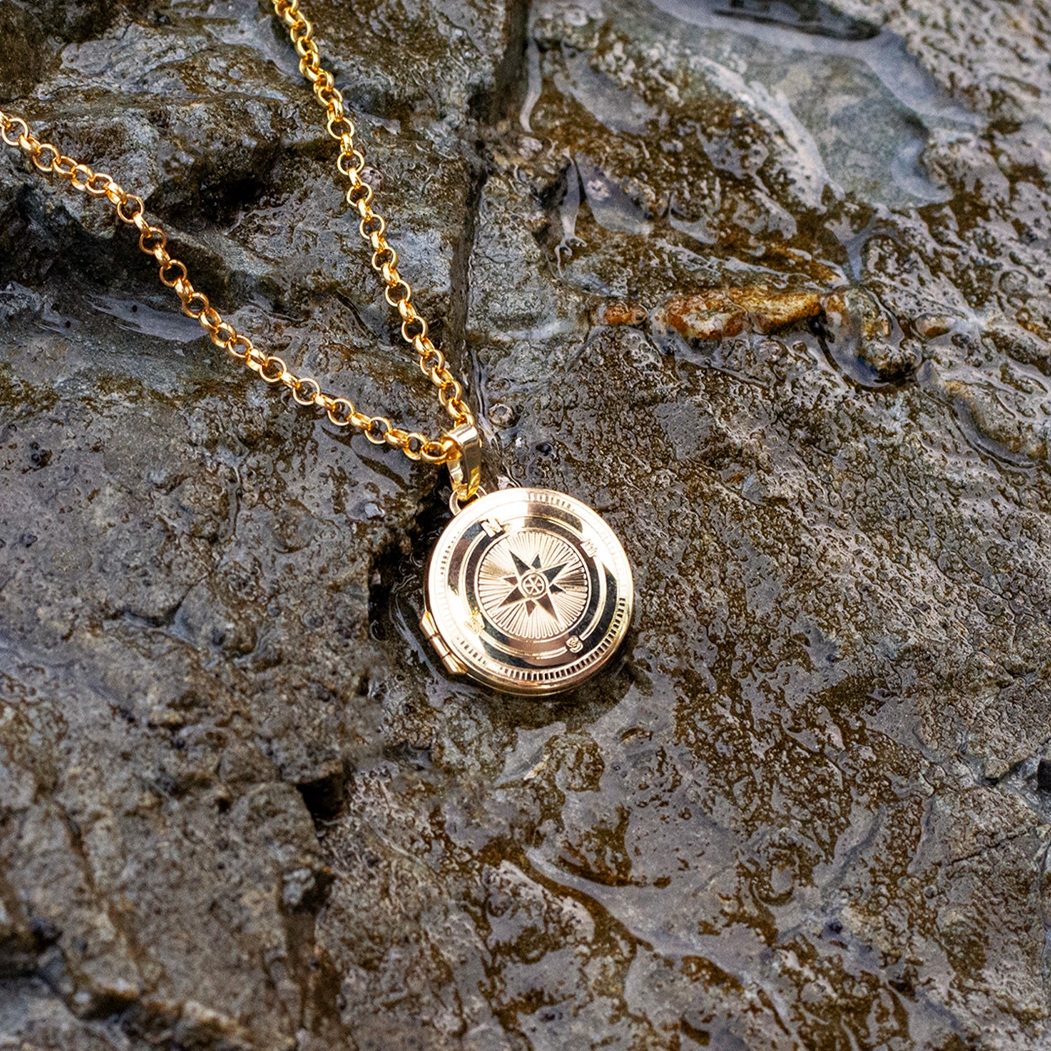 Gold necklace with a compass detail pendant on a stone surface