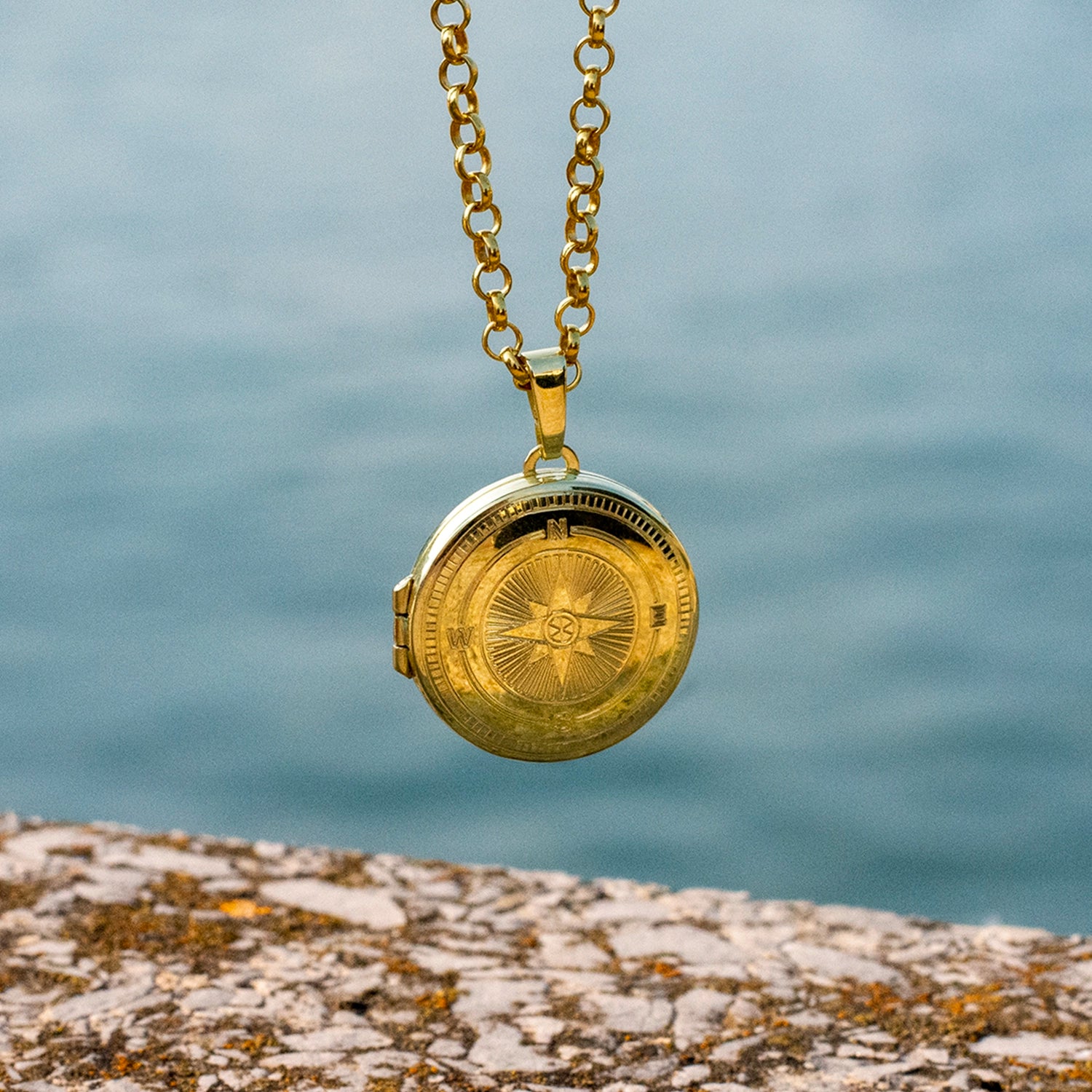 Gold locket necklace on a chain with a blurred water background