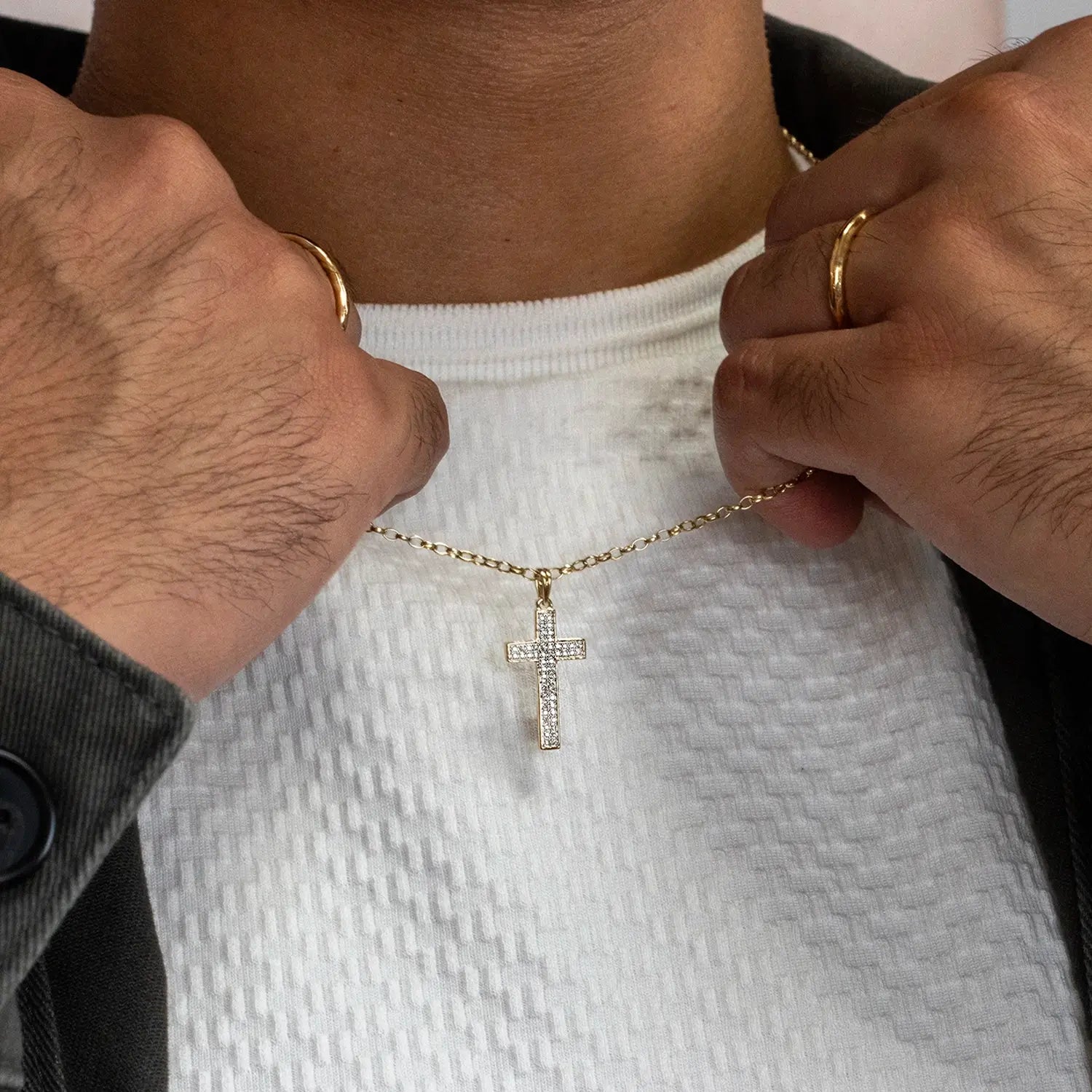 Gold diamond cross necklace being adjusted on a person wearing a white shirt.