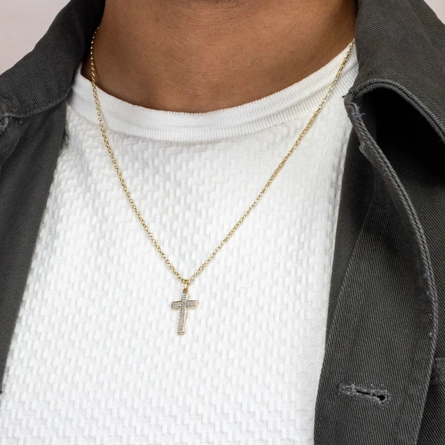Gold diamond cross necklace worn by a person with a white shirt and gray jacket.