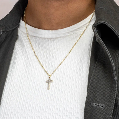 Gold diamond cross necklace worn by a person with a white shirt and gray jacket.