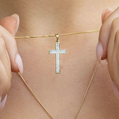 woman wearing gold diamond cross necklace, sturdy gold curb chain, high polish finish, small shiny diamonds, religious Christian pendant for men and women, holding chain