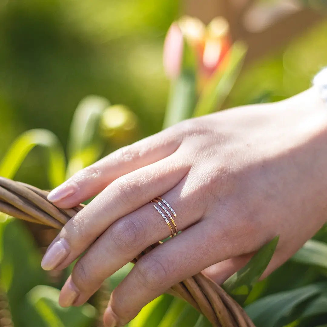 Hand wearing a 9ct solid gold spiral ring featuring three slender bands, two with pavé-set diamonds, resting on a wicker basket in soft natural light.