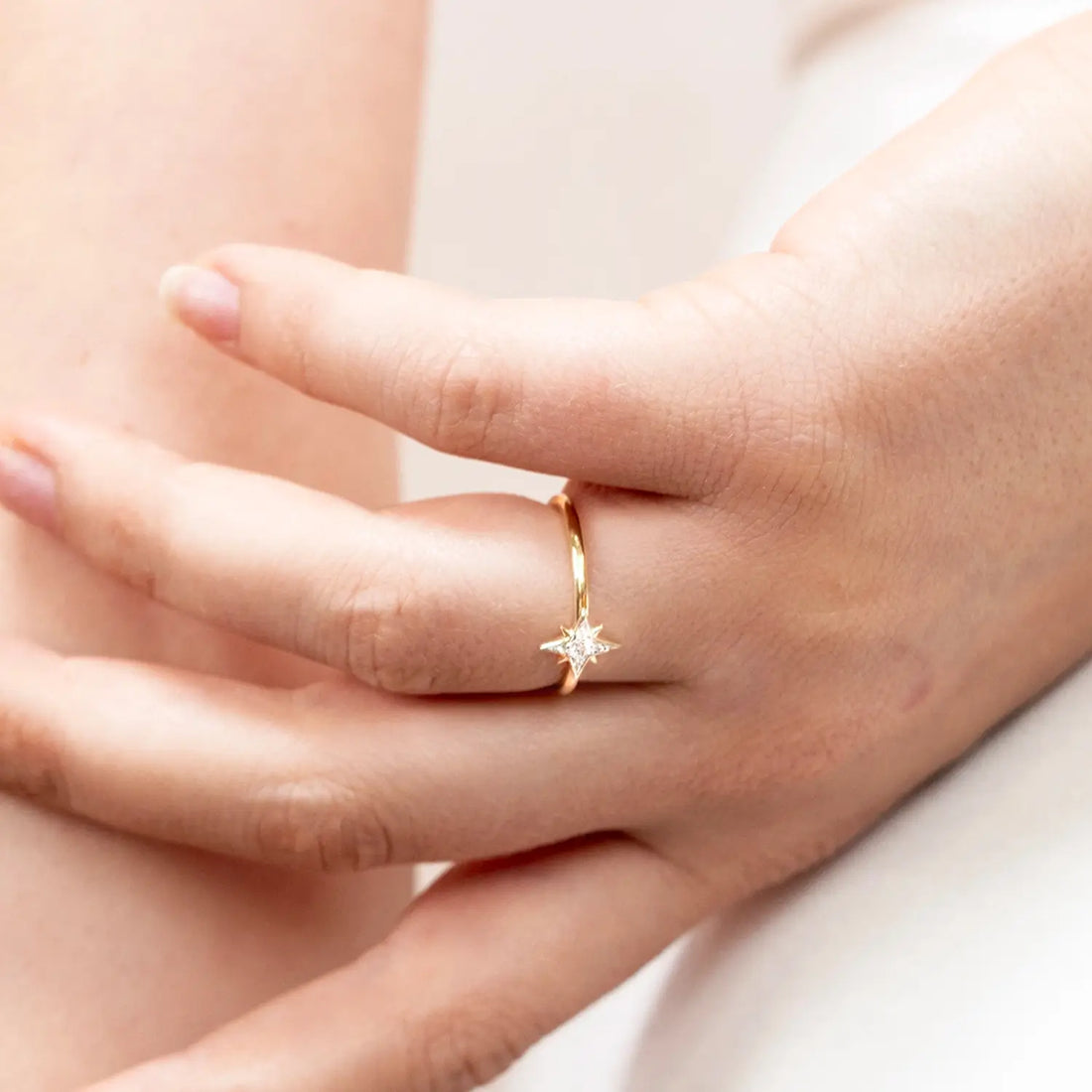 Hand wearing a gold ring with a star design on a plain background