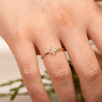 Close-up of a hand wearing a delicate 18ct gold vermeil diamond star ring, featuring a sparkling star-shaped setting on a fine polished band against a softly blurred floral background.