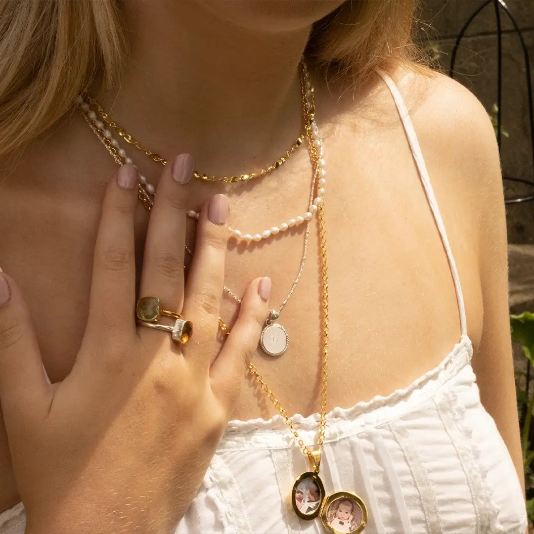 Woman wearing layered gold and silver necklaces including a personalised engraved disc pendant and an open gold locket with photos inside.