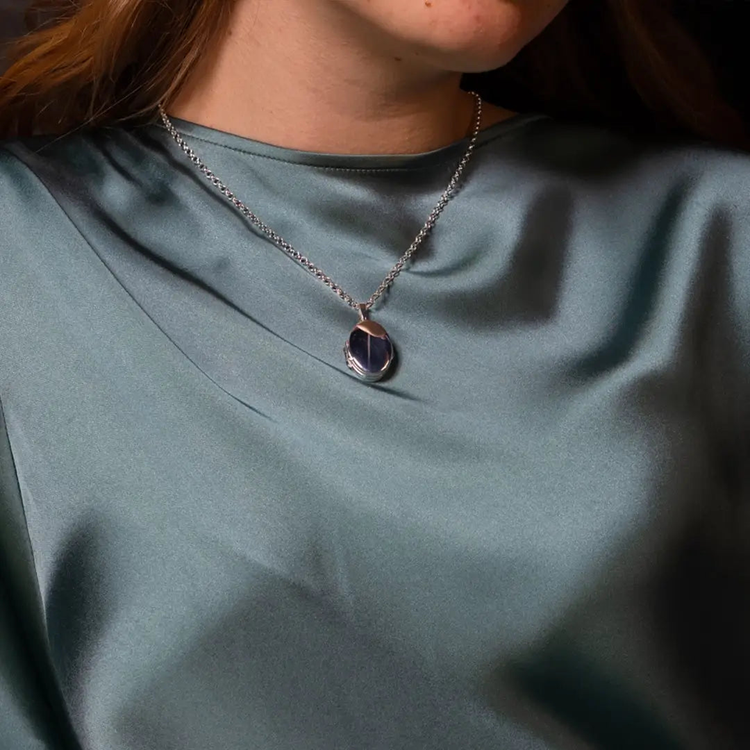 Closed sterling silver oval locket necklace worn on a model, high-polish finish reflecting light against a soft green satin top.