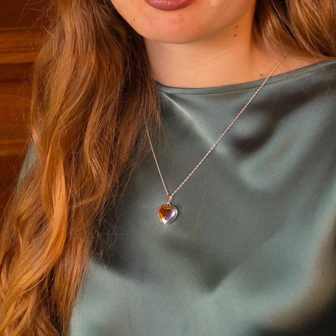 Closed sterling silver heart locket necklace worn on a model, high-polish finish reflecting light against a soft green satin top.