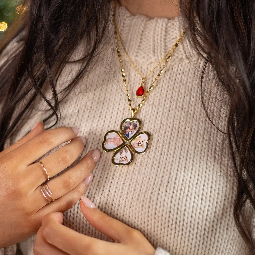 Gold four-photo heart locket necklace worn layered with a garnet pendant, showing personalised photo inserts against a cream knit jumper.