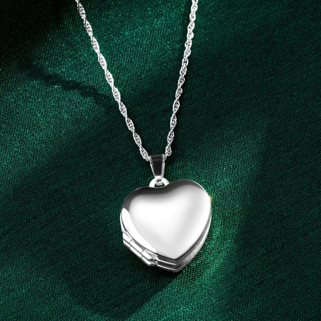 Sterling silver heart locket necklace on a delicate chain, photographed on rich green silk fabric with the polished heart pendant closed.