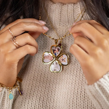 lose-up of a person holding a gold four-heart clover-shaped locket necklace, each heart displaying 4 photos inside inside, worn over a cream knit sweater.
