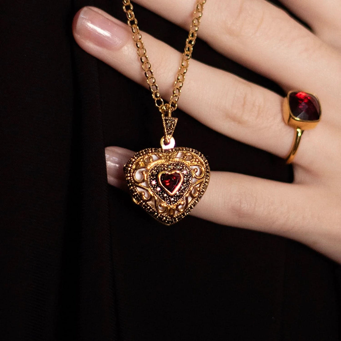 Model wearing ornate gold heart locket necklace with red garnet stone and matching garnet ring