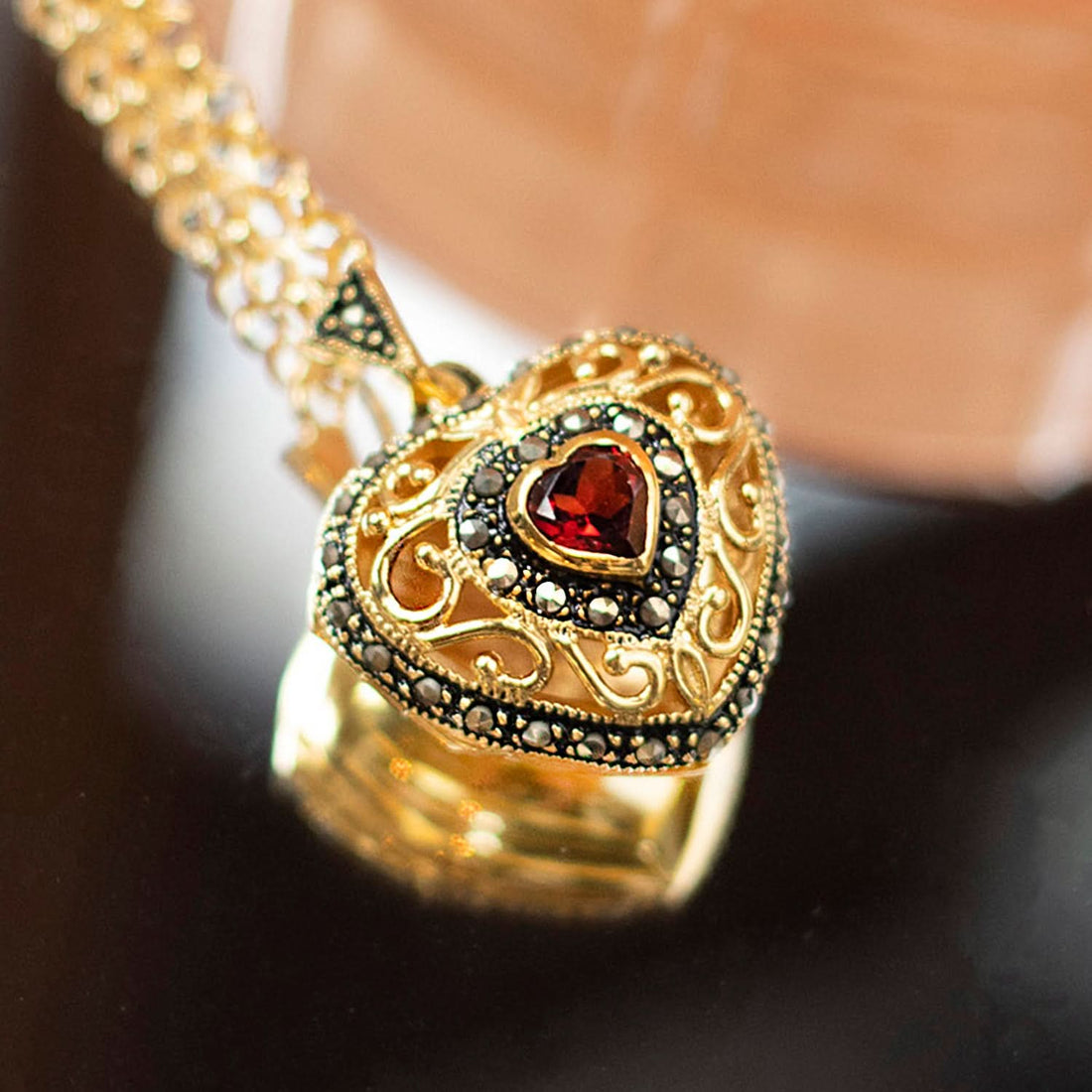 Close-up of ornate gold heart locket necklace with red garnet gemstone and black marcasite detailing