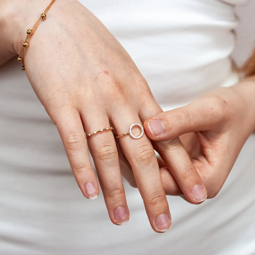 Close-up of a hand wearing a 9ct solid gold open circle diamond ring with a pavé-set diamond halo, styled alongside a delicate diamond band and a gold bead bracelet.